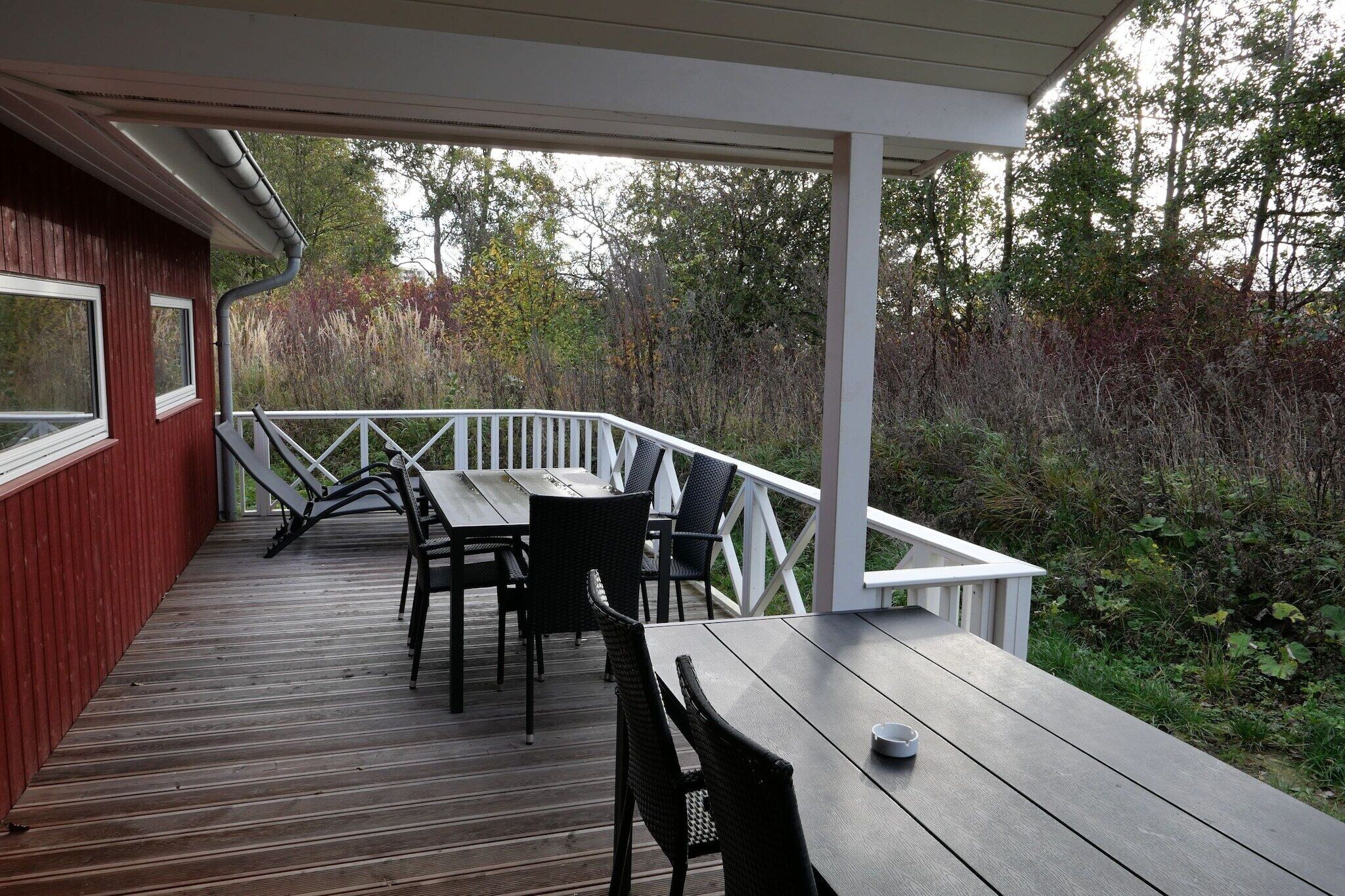 A covered outdoor deck with a table and chairs, surrounded by white railings and a wooden floor.