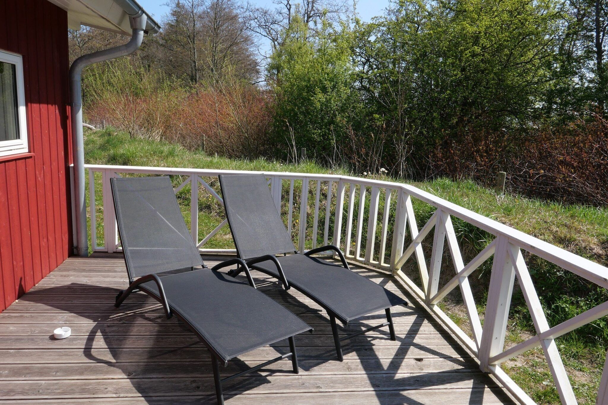 A wooden deck with two lounge chairs and a white railing.