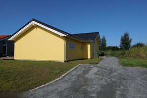 En gul bygning med saddeltag, en belagt indkørsel og en grøn græsplæne.