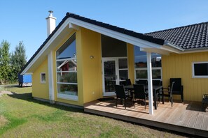 A yellow house with a large glass door and a patio with outdoor furniture. - Großer Familienaufenthalt am Strand (Großenbrode)