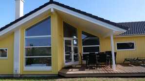 Keltainen rakennus, jossa on katettu terassi, suuret ikkunat ja savupiippu.