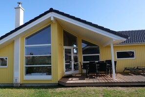 Ein gelbes Gebäude mit überdachter Terrasse, großen Fenstern und Schornstein.