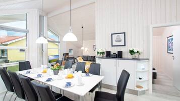 Een moderne eetruimte met een witte tafel voor vier personen, zwarte stoelen en hanglampen.
