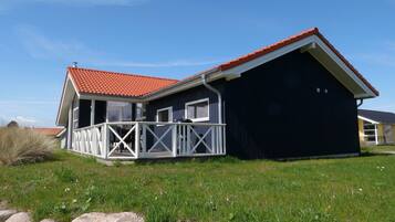 Een twee verdiepingen tellend huis met een dak van rode tegels, een balkon met witte leuningen, en een donkere buitenmuur.