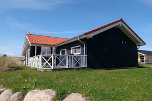 Ein zweistöckiges Haus mit rotem Ziegeldach, einem Balkon mit weißen Geländern und einer dunkel gestrichenen Außenwand.
