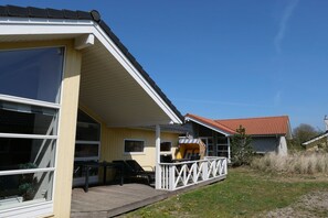Ein Haus mit überdachter Veranda, einem Essbereich mit Gartenmöbeln und einem roten Ziegeldach.
