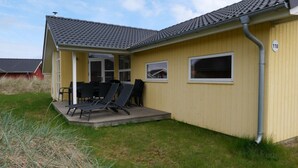 En gul byggnad med ett grått tak täckt med takpannor, en inglasad uteplats med stolar och en skylt med siffran ’118’.
