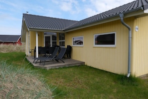 A yellow building with a grey tiled roof, a covered patio with chairs, and a number '118' sign. - Geräumiger Familienaufenthalt am Strand (Großenbrode)