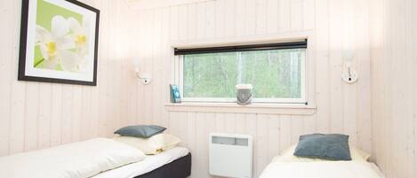 A room with two beds, a window with a view of greenery, a radiator, and a framed picture on the wall.