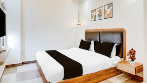 Quarto de hotel moderno com uma cama grande, mesa de cabeceira com um vaso de flores e televisão na parede.
