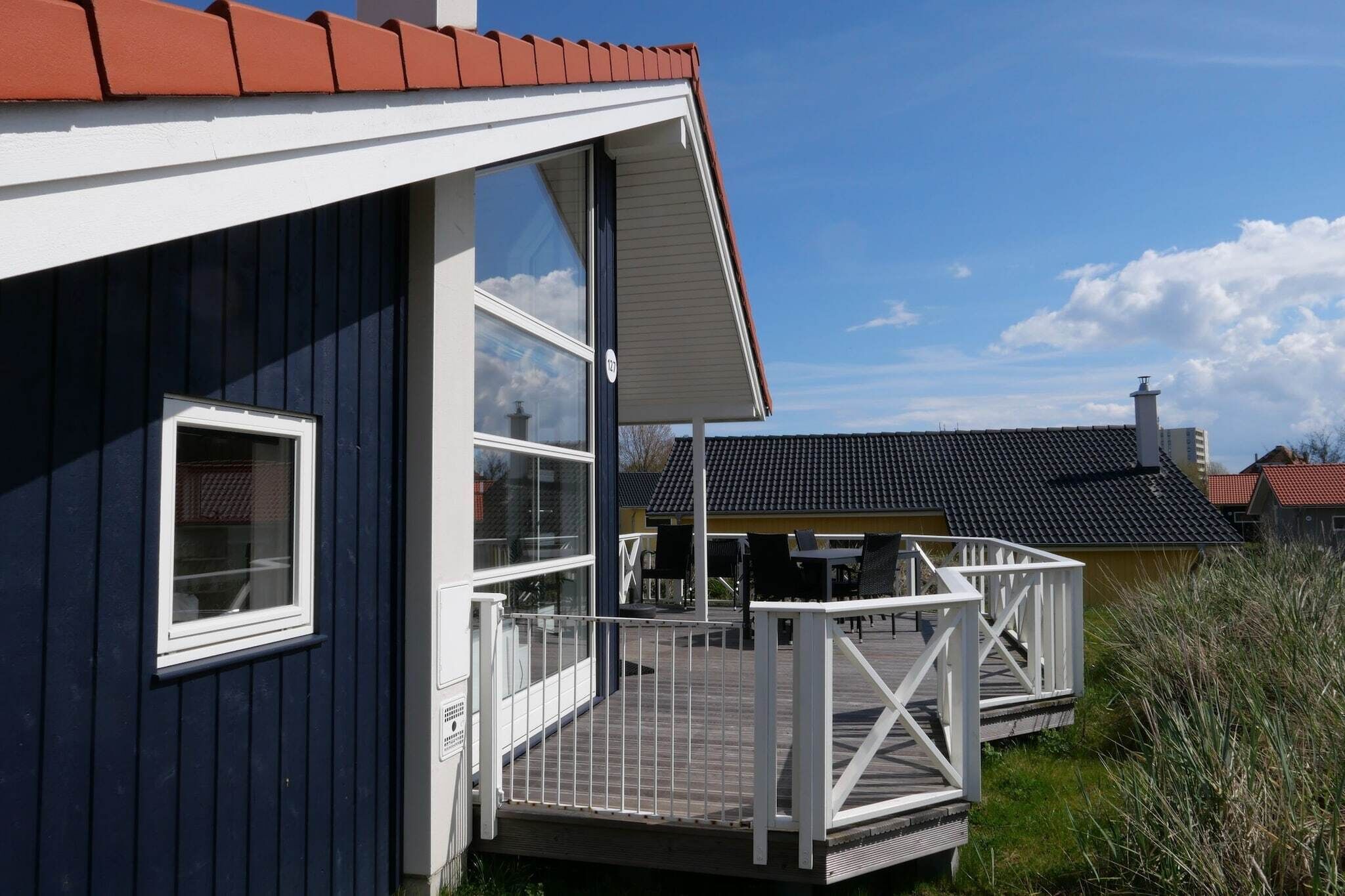 A building with a dark blue exterior, white trim, and a red roof. There is a deck with outdoor furniture and a railing.