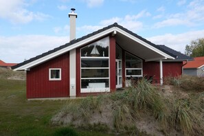A red single-story house with a sloped roof, a chimney, and a large glass door. - Serene Wellness Lodge für 8 Personen (Großenbrode)