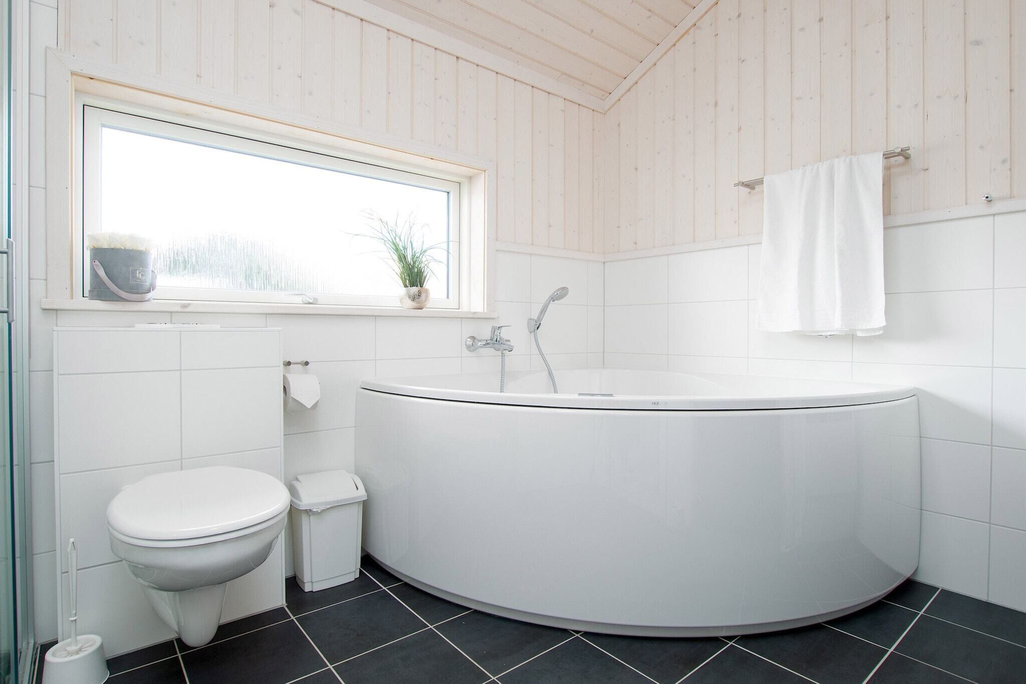 A modern bathroom with a freestanding bathtub, a toilet, and a window with a plant.