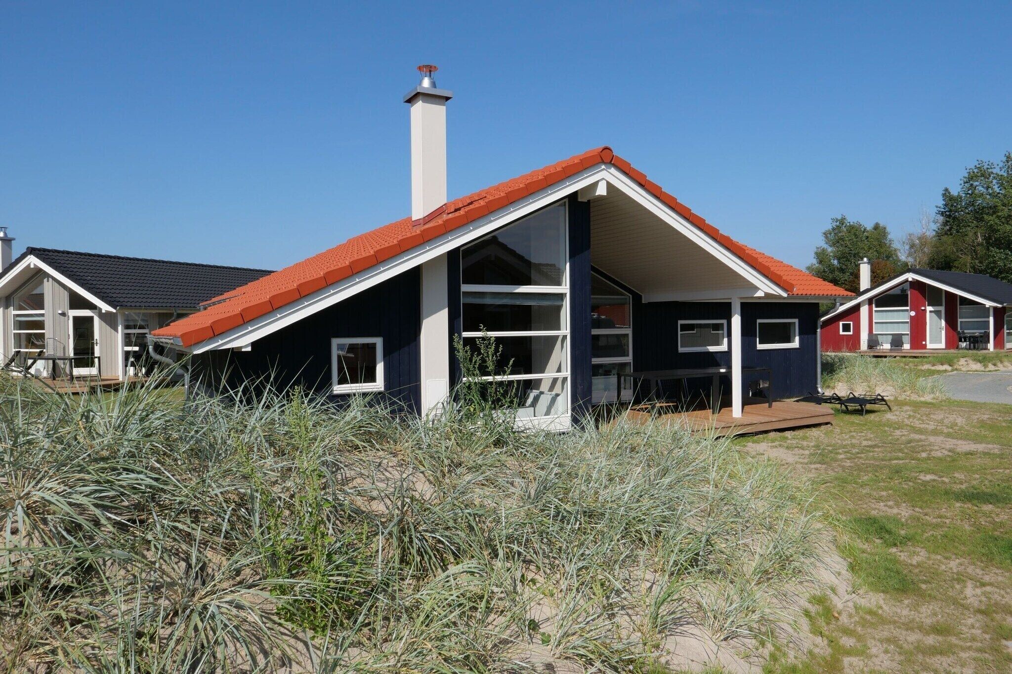 A modern house with a red roof, large windows, and a chimney.