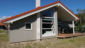 En envåningsbyggnad med ett rött tak, ett stort fönster och en uteplats med utemöbler.