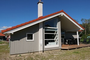 A single-story building with a red roof, a large window, and a deck area with outdoor furniture. - Großenbrode Meeresflucht (Großenbrode)