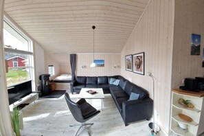 A modern living room with a sectional sofa, a flat-screen TV, a dining table, and a fireplace. - Skandinavisches Haus für 10 (Großenbrode)