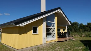 A yellow building with a large window, a chimney, and a deck area. - Küsten-Spa-Haus für 10 Personen (Großenbrode)