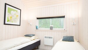 A room with two beds, a window with a view of trees, a radiator, and a framed picture on the wall. - Küsten-Spa-Haus für 10 Personen (Großenbrode)