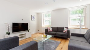 Ein modernes Wohnzimmer mit Flachbildfernseher, grauen Sofas, einem Glastisch und einer Topf-Orchidee.