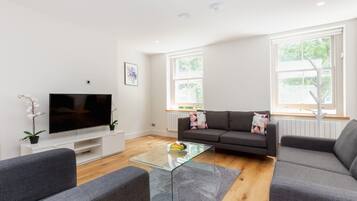 A modern living room with a flat-screen TV, grey sofas, a glass coffee table, and a potted orchid.