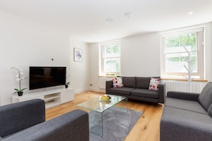 A modern living room with a flat-screen TV, grey sofas, a glass coffee table, and a potted orchid. - Spacious 2BR 2BA Fitzrovia close to Bloomsbury (London)