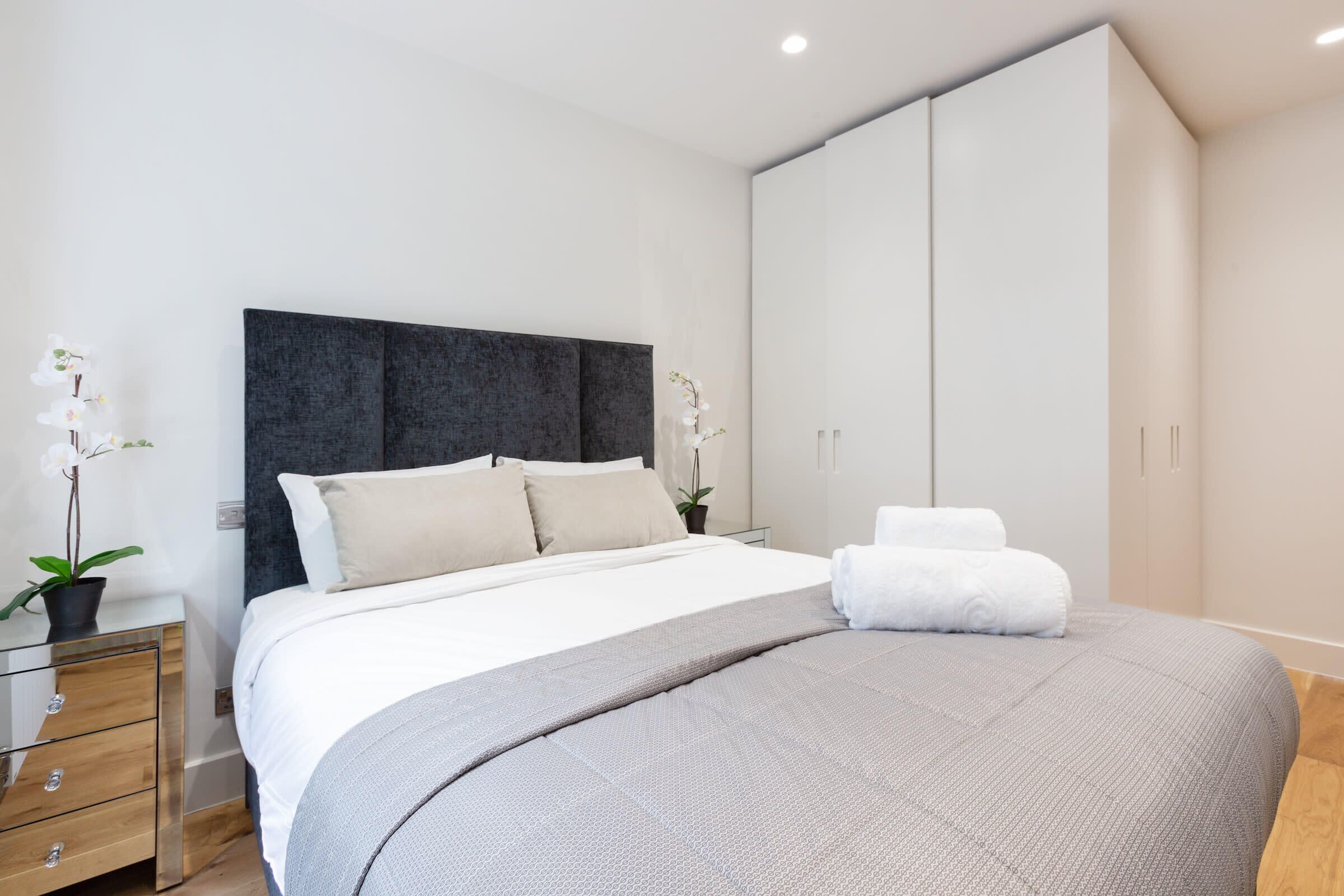 A modern bedroom with a large bed, a bedside table with a lamp, and a wardrobe.