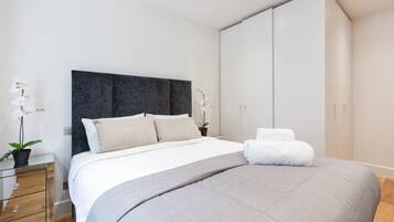 A modern bedroom with a large bed, a bedside table with a lamp, and a wardrobe.