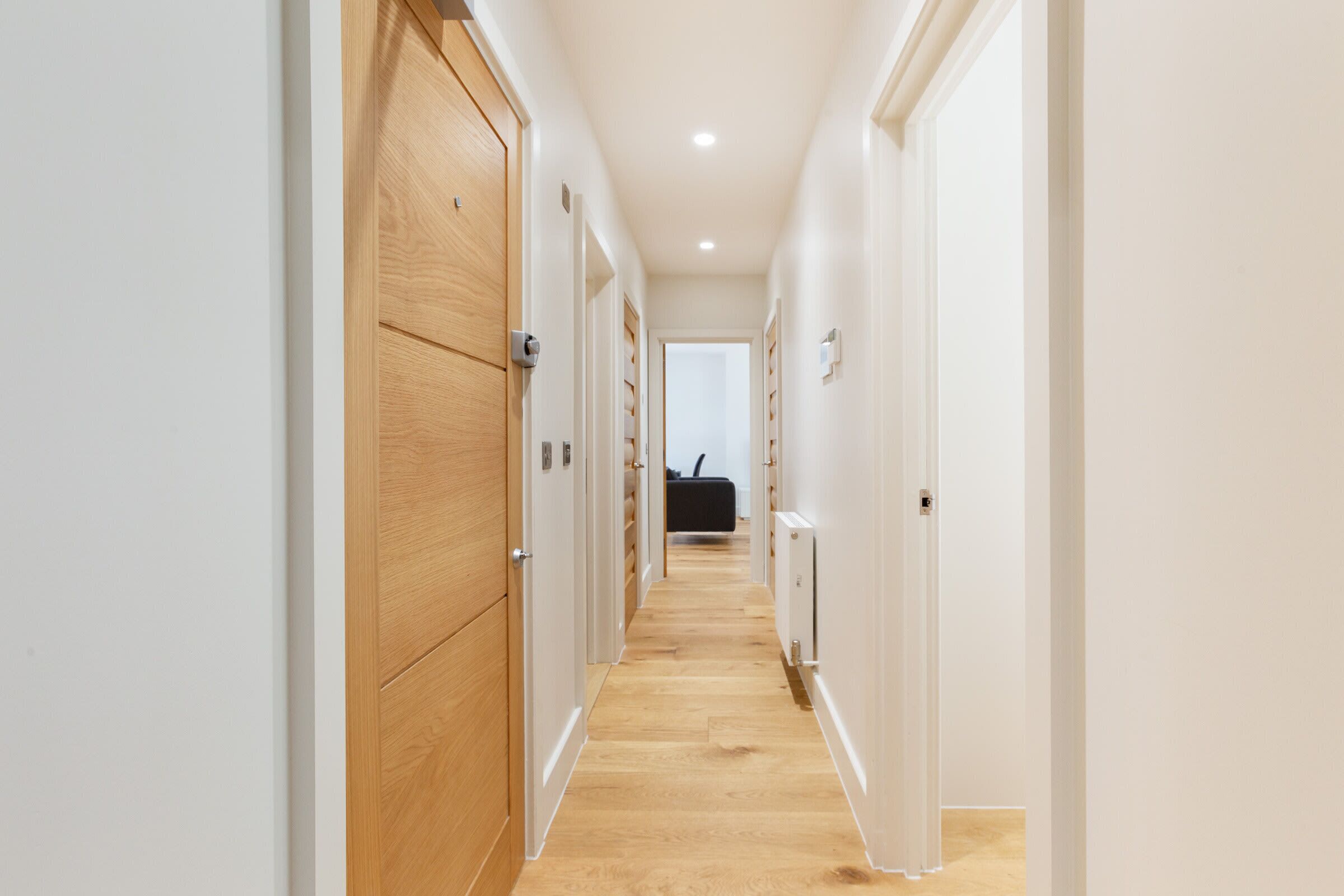 Un pasillo con puertas de madera y paredes blancas que conduce a una habitación con una silla negra y un radiador.