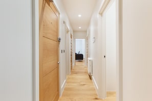 A hallway with wooden doors and white walls, leading to a room with a black chair and a radiator. - Spacious 2BR 2BA Fitzrovia close to Bloomsbury (London)