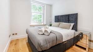 Ein modernes Schlafzimmer mit einem großen Bett, einem Fenster und einem Nachttisch.
