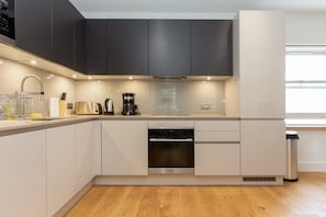 A modern kitchen with a dishwasher, oven, and coffee maker. - Spacious 2BR 2BA Fitzrovia close to Bloomsbury (London)
