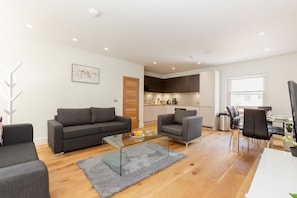 A modern living room with a sofa, armchairs, a glass coffee table, and a dining area with chairs and a table. - Spacious 2BR 2BA Fitzrovia close to Bloomsbury (London)