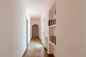 A hallway with a tiled floor, white walls, and a bookshelf with books. - Villa Marina, an authentic Mediterranean home overlooking the sea of Villasimius (VILLASIMIUS)