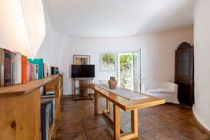 Ein Zimmer mit einem Holztisch, einem Fernseher, einem Bücherregal und einem Fenster.