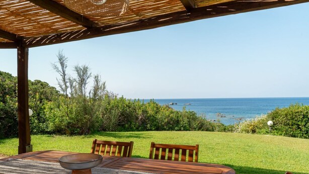 An outdoor dining area with a view of the sea, wooden furniture, and a pergola structure. - Villa Marina, an authentic Mediterranean home overlooking the sea of Villasimius (VILLASIMIUS)