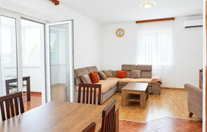 A modern living room with a sofa, a dining table, and chairs. There is a clock on the wall and an air conditioning unit. - 3 bedroom stunning apartment in Pula (Pula)