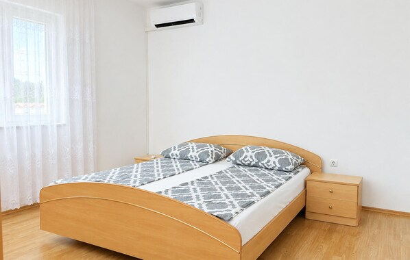 Een eenpersoonsbed met houten frame, twee kussens, een nachtkastje en een wandairconditioner.