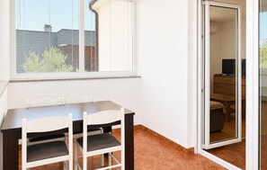 Een eethoek met een tafel en stoelen, een schuifdeur naar een woongedeelte en een raam met jaloezieën.