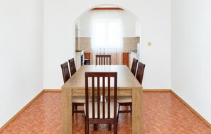 Een eethoek met een houten tafel en stoelen, een keuken op de achtergrond en een betegelde vloer.
