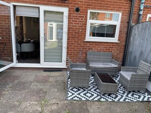 Ein Patio mit Korbmöbeln, einem gemusterten Teppich und einer Glastür, die zu einem Innenbereich führt.