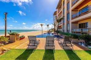 Uma área à beira da piscina com espreguiçadeiras, um deck de madeira e vista para a praia.
