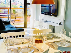 A dining area with a table set for two, a sofa, and a TV in the background. - Deluxe Beachfront Apartment with Fantastic View and Infinity Pool (Caucaia)
