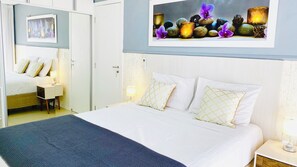 Una habitación de hotel con cama, mesitas de noche, televisor de pared y un cuadro enmarcado sobre la cama.