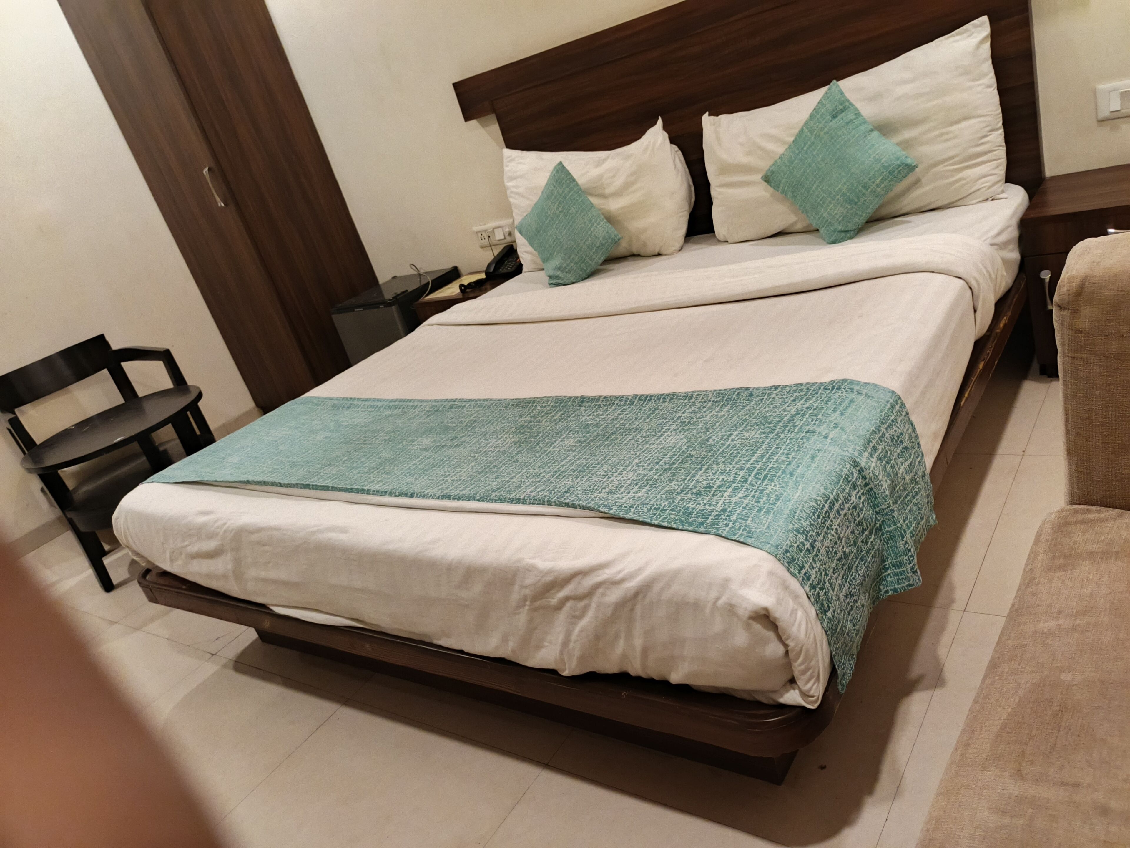 Uma cama com cabeceira de madeira, roupa de cama branca e manta azul-turquesa.