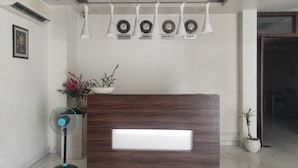 A reception desk with a wooden finish, a potted plant, and a wall-mounted clock with city names. - DREAM INN (Lucknow)