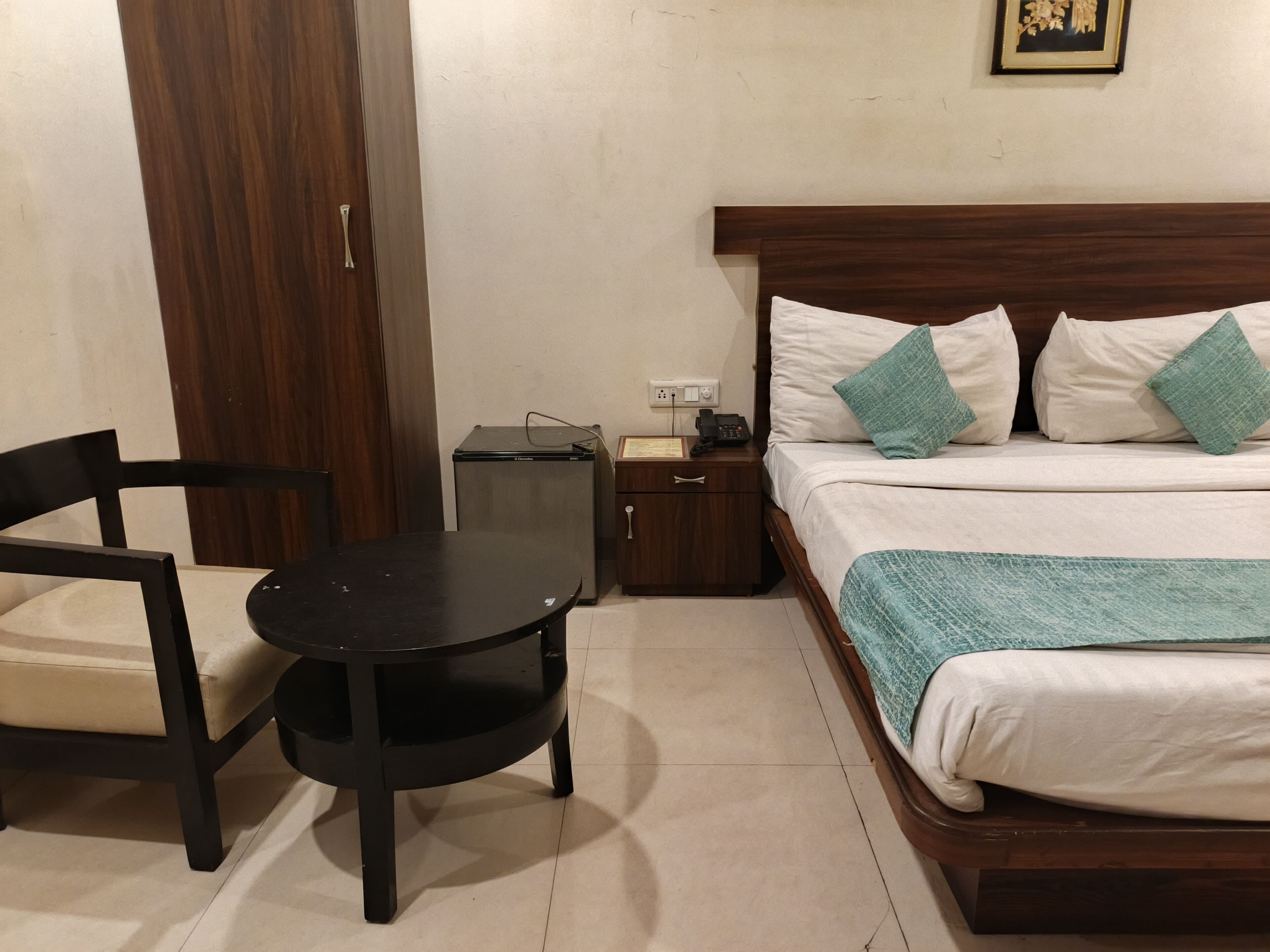 A hotel room with a bed, bedside table, chair, and a small desk with a telephone.
