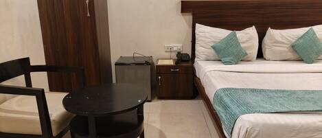 A hotel room with a bed, bedside table, chair, and a small desk with a telephone.