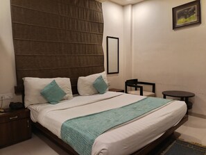 A hotel room with a large bed, a nightstand, a small table, and a chair. - DREAM INN (Lucknow)