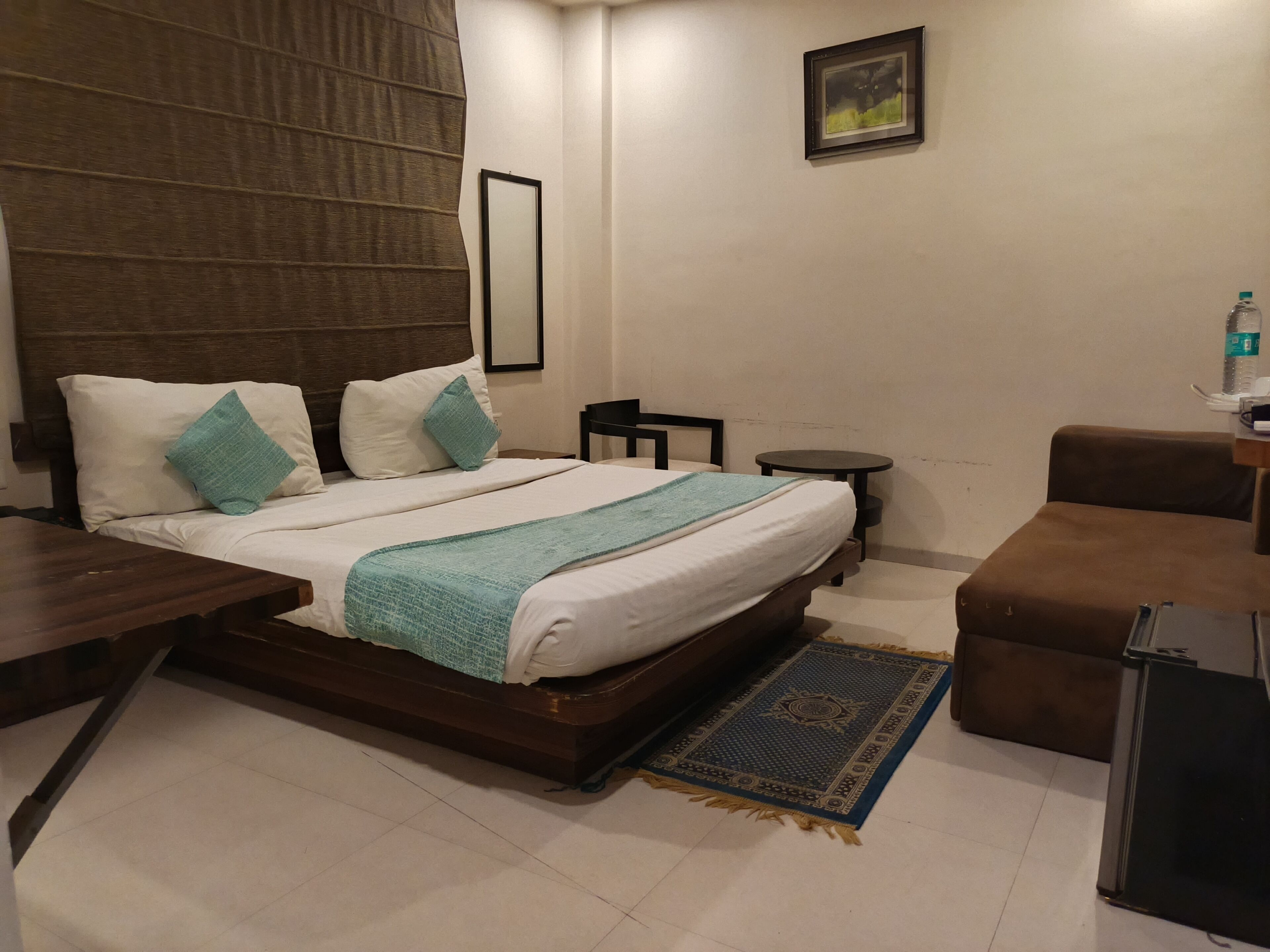 A hotel room with a bed, bedside tables, a small round table, a chair, and a sofa.